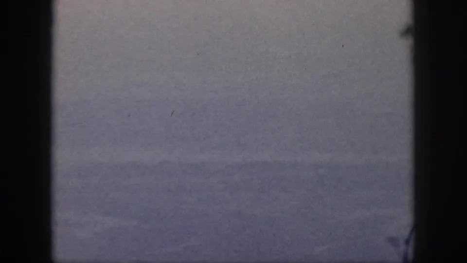 A distant, hazy Oahu aerial view is visible through a passenger window, with aged color and light film specks.