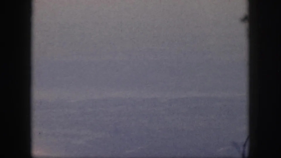 1959 Oahu home-movie frame with a low ocean horizon, pale sky, and heavy dark edging from the camera or window view.