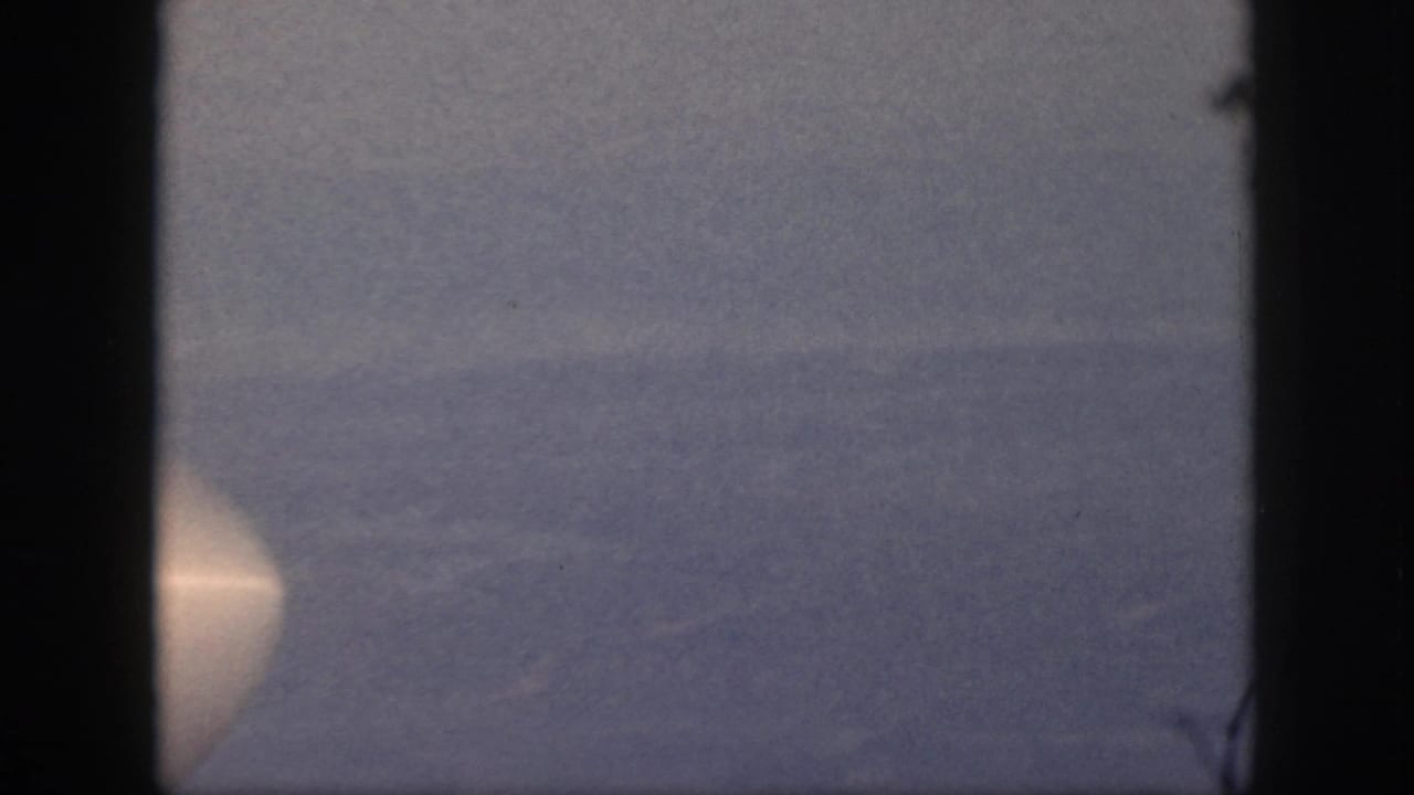 1959 Oahu 8mm still showing calm water, a distant horizon, and a bright circular light at the lower left edge.