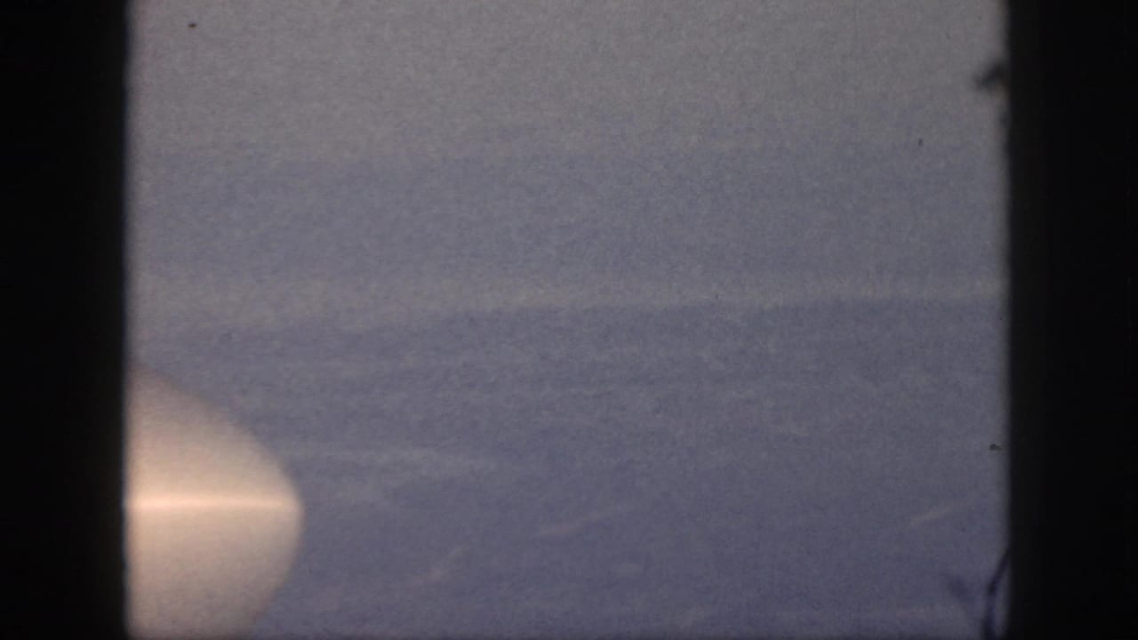 1959 Oahu home-movie frame of a calm ocean horizon with a bright circular light near the lower left edge.
