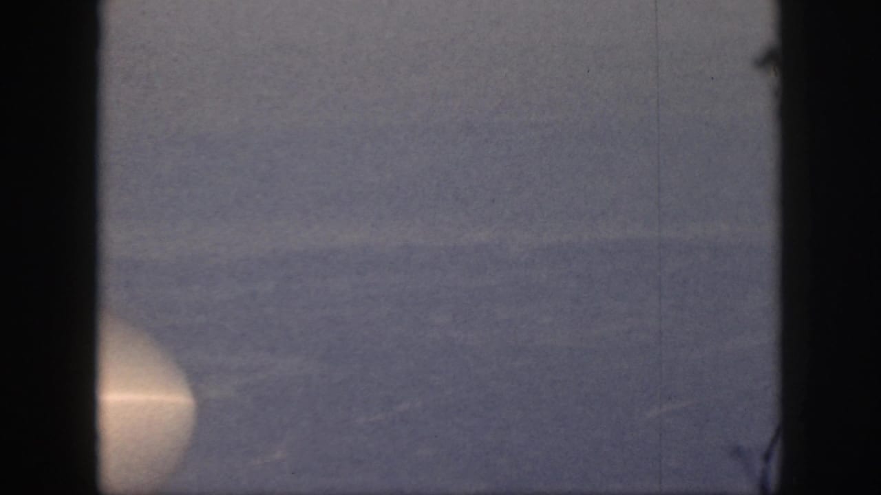 1959 Oahu home-movie frame showing a fog-covered valley with dark window-like borders and a faint bright glow at left.