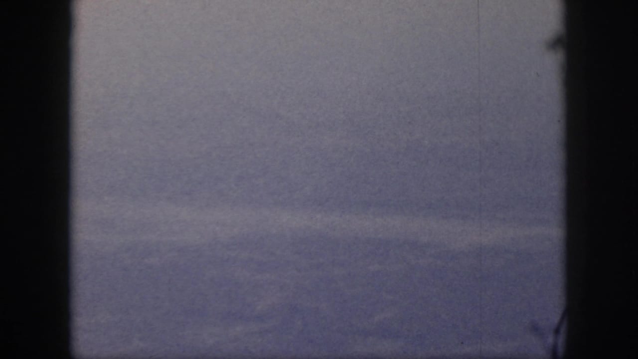 1959 Oahu home-movie frame showing a hazy valley or hillside through a dark bordered view, with visible grain and surface marks.