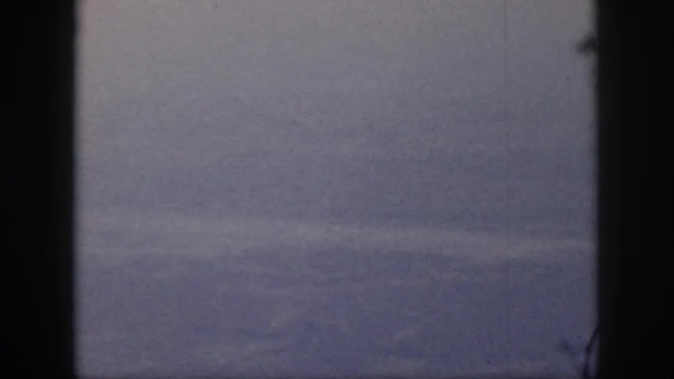1959 Oahu home-movie frame showing a hazy valley or hillside through a dark bordered view, with visible grain and surface marks.