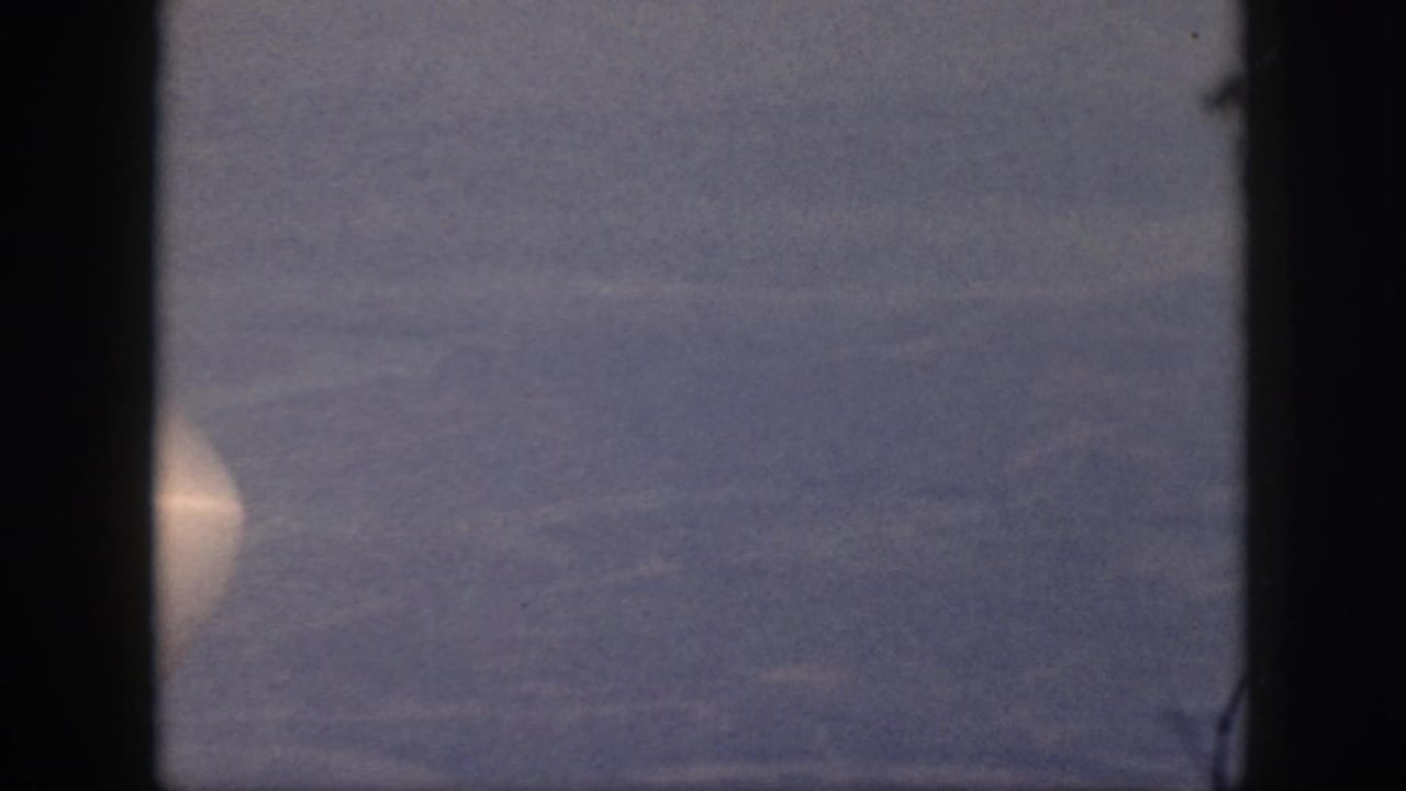 Airplane window framing a hazy aerial view with a pale aircraft shape near the left edge.