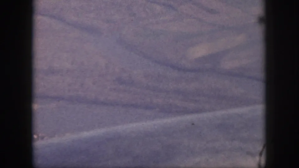 Oahu aerial view from a 1959 home movie, showing water, a faint shoreline, and inland terrain through purple-tinted 8mm grain.