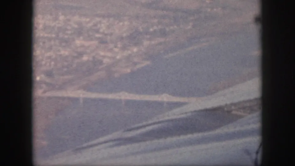 1959 Oahu 8mm aerial view with a bridge over a broad waterway and distant shoreline seen through an airplane window.