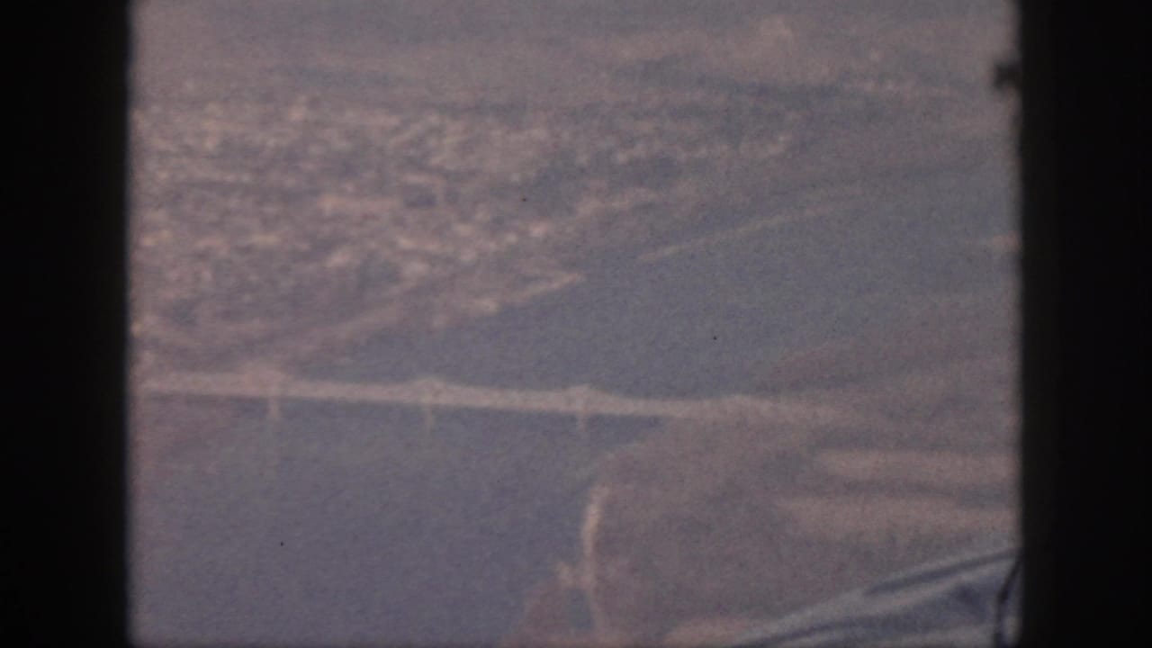 Soft 8mm aerial view from Oahu in 1959, with a bridge over water and land forms receding into haze.