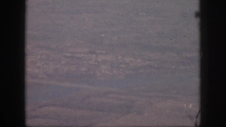 1959 Oahu home-movie frame showing a soft, purple-tinted aerial view of land or water through dark window-like bars.