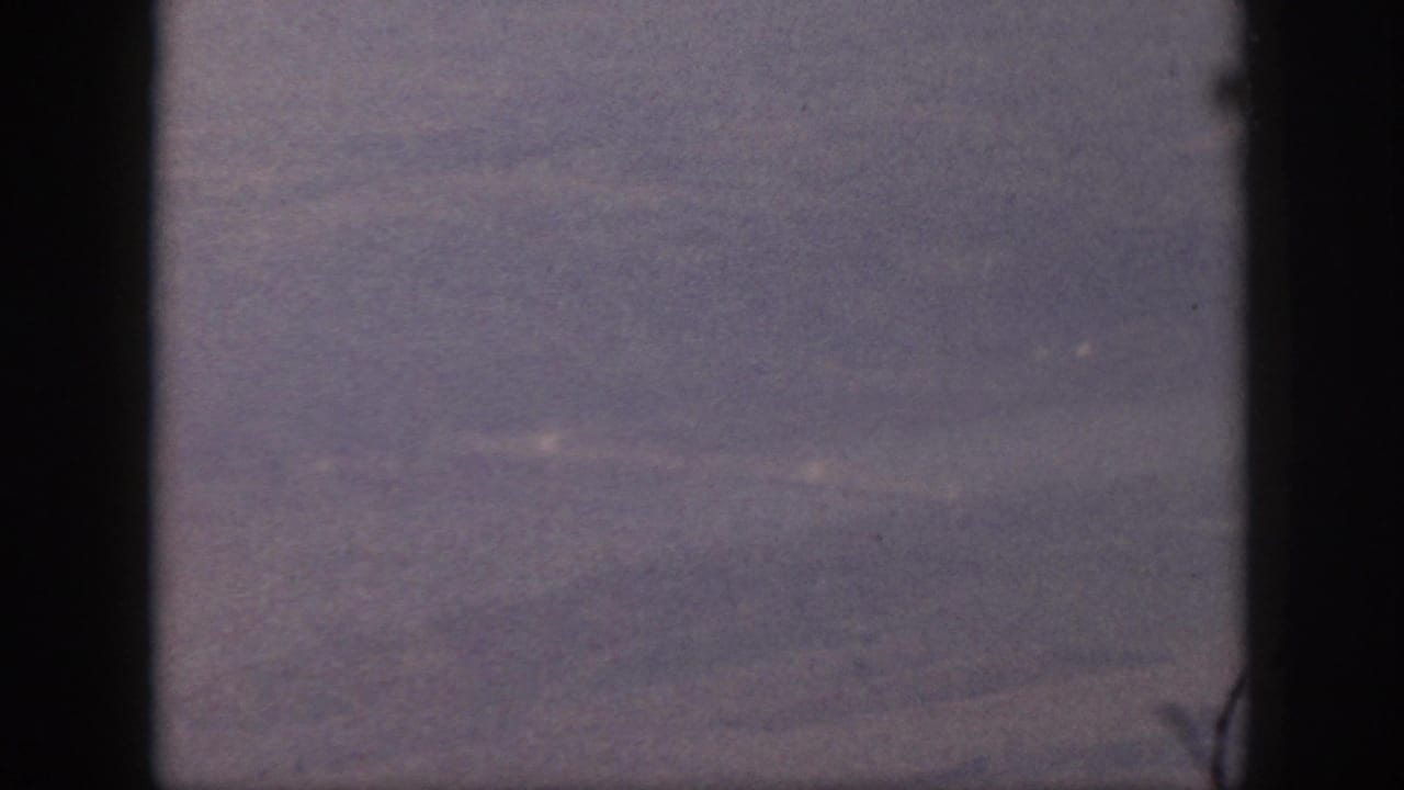 Soft aerial terrain with dark frame bars and heavy grain.