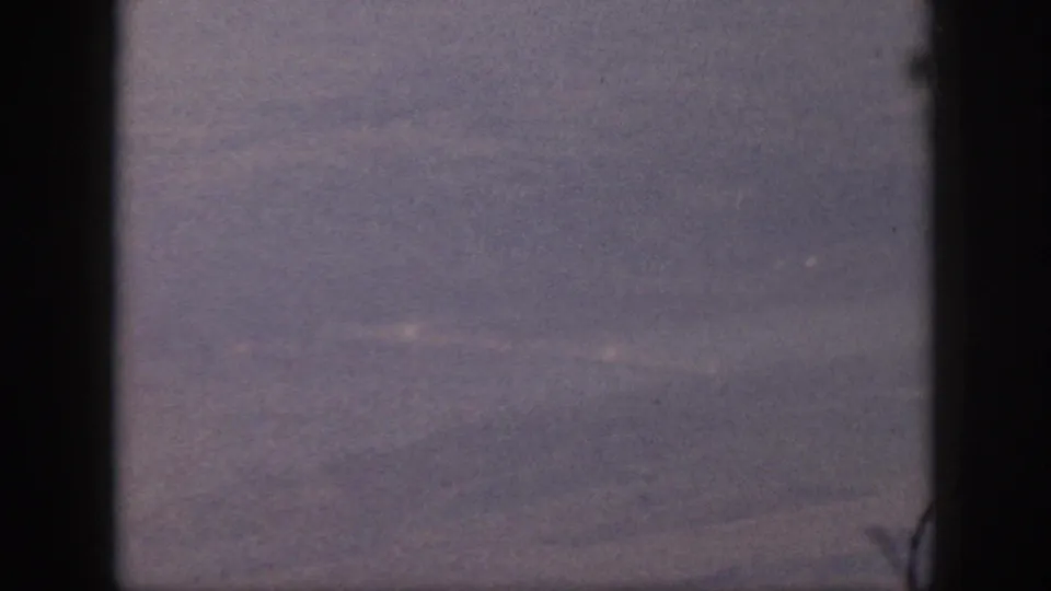 A grainy 8mm aerial view over Oahu, with indistinct ground forms and dark vertical edges framing the shot.