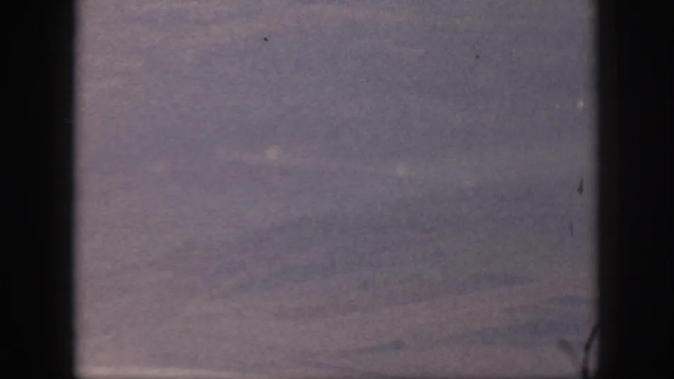 Hazy 1959 Oahu sky view with faint cloud or contrail lines, framed by visible 8mm film edges.