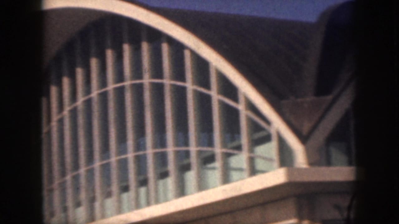 Closer 1959 Oahu view of an airport terminal exterior with tall curved glazing and a sweeping arched roof.
