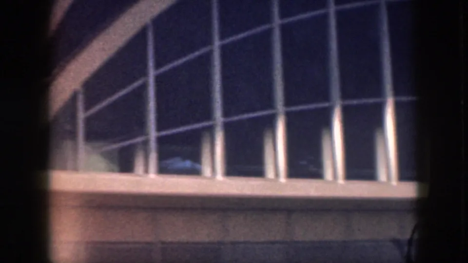 1959 Oahu home-movie frame of a modern exterior with tall window panes, white vertical supports, and a curved roof edge.