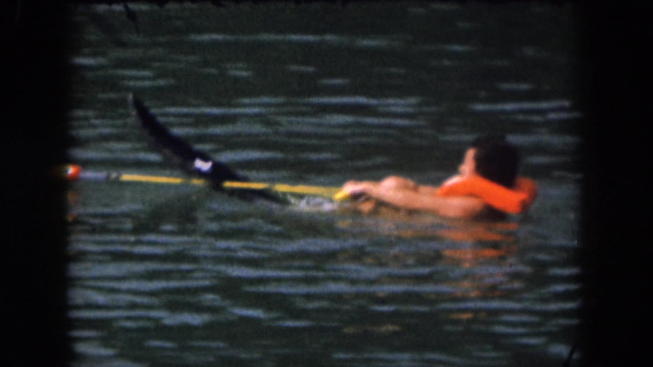 Person in orange life preserver stretched forward in lake water while holding the tow rope.