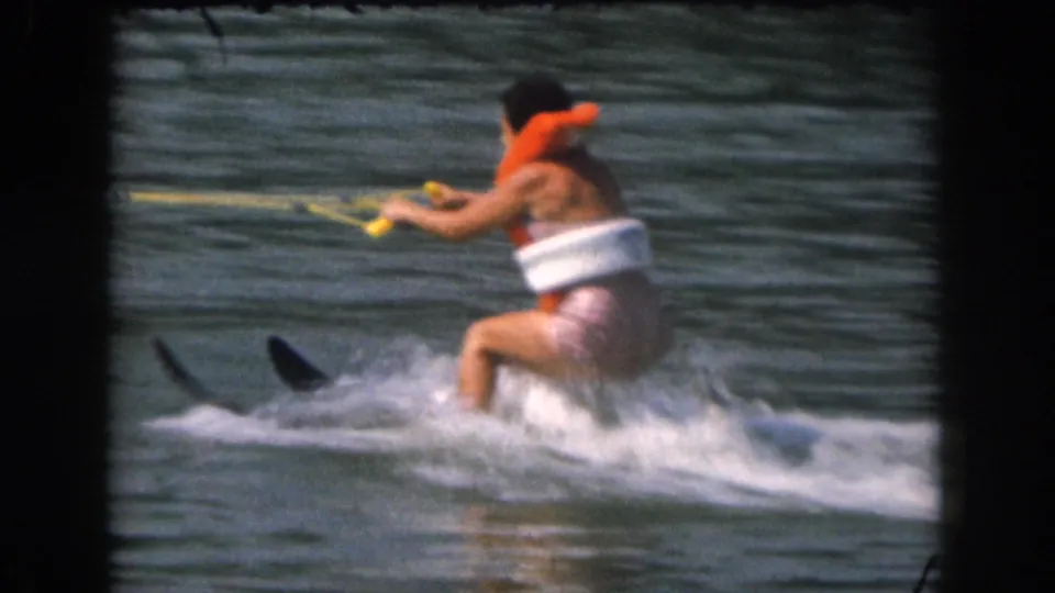 1961 Grand Rapids home-movie frame showing the skier lifting onto water skis as spray breaks around their legs.