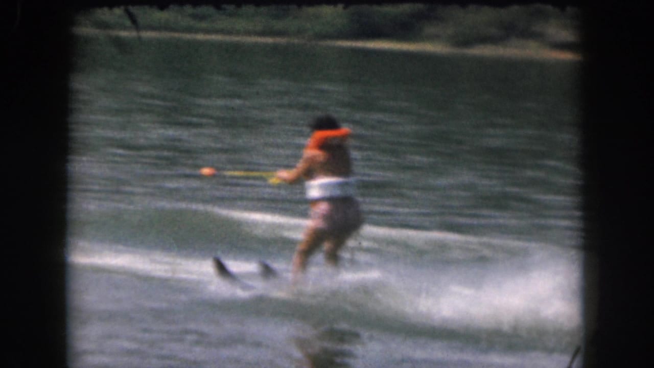 1961 Grand Rapids-area 8mm home-movie frame of a distant water skier in an orange life vest crossing open lake water.