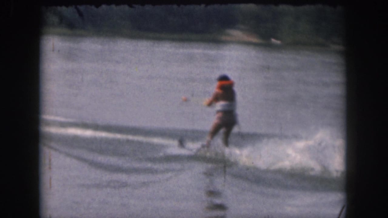 Distant water skier continues across open water with a white wake trailing behind.