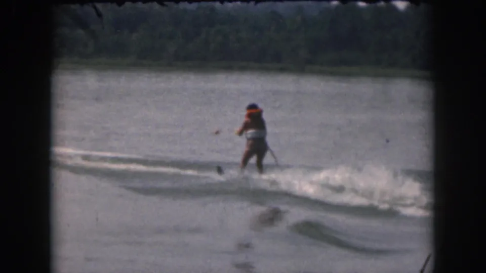 8mm home-movie frame from 1961 showing a water skier on a Michigan lake with a tree-lined shore beyond.