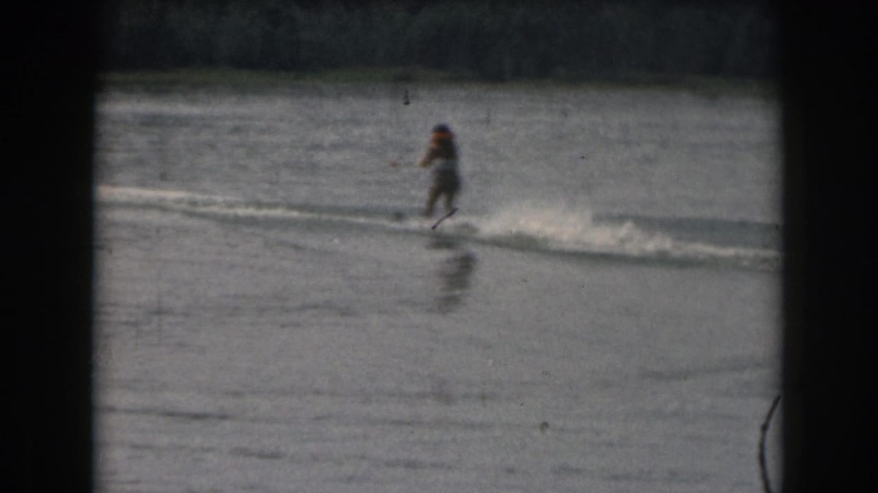 Water skier glides across a calm lake behind a boat wake.