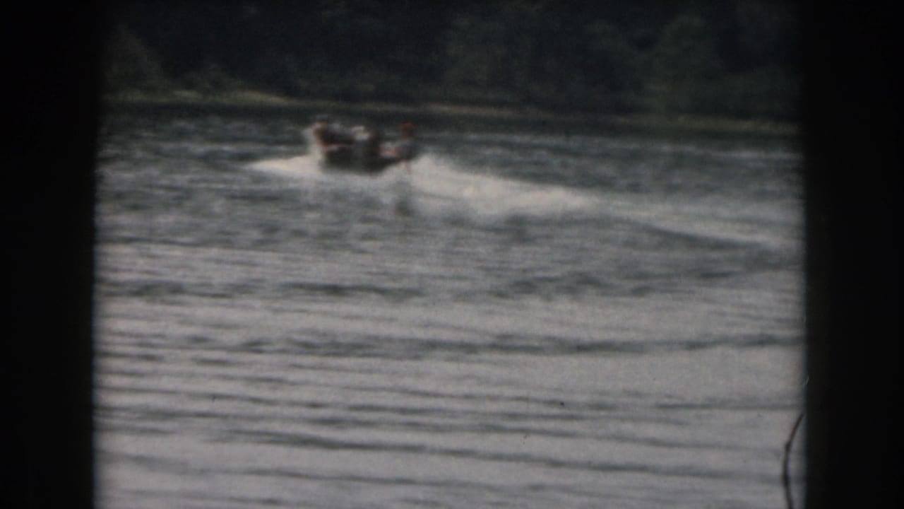 1961 Grand Rapids, Michigan 8mm frame showing a distant motorboat towing a water skier across a tree-lined lake.
