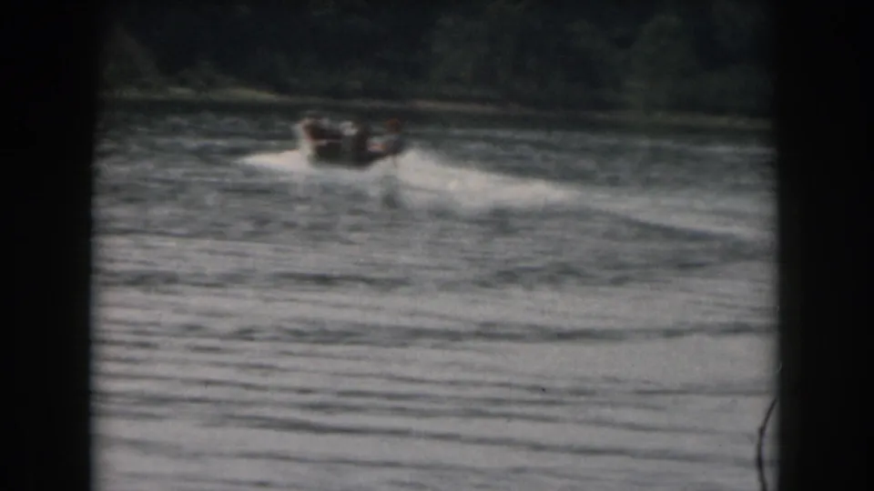 1961 Grand Rapids, Michigan 8mm frame showing a distant motorboat towing a water skier across a tree-lined lake.