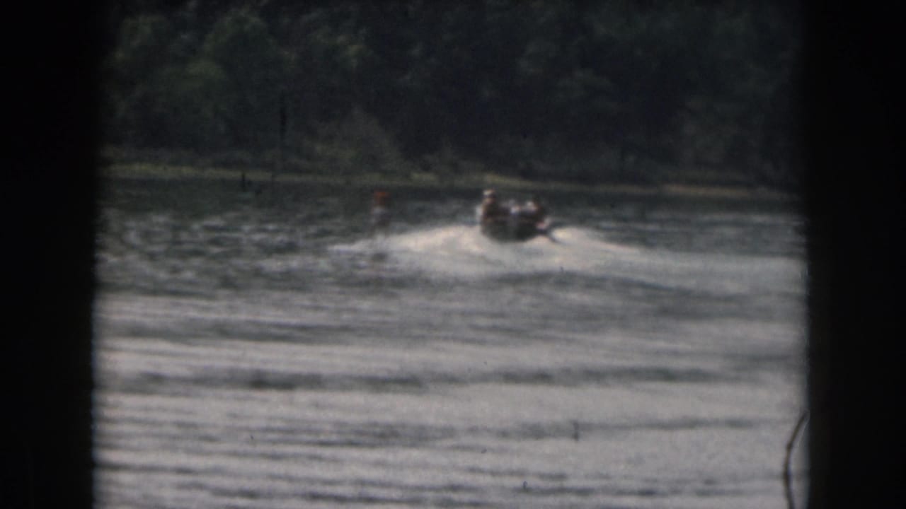 Motorboat and water skier continue across rippled lake water with trees in the background.