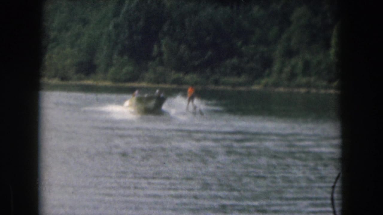 Grand Rapids, Michigan 1961 home movie frame showing a water skier following a small motorboat on a wooded lake.