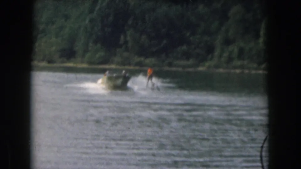 Grand Rapids, Michigan 1961 home movie frame showing a water skier following a small motorboat on a wooded lake.