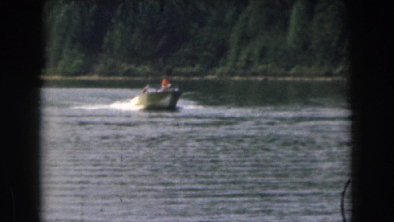 1961 Michigan 8mm frame with a small motorboat crossing lake water, its wake bright against the wooded background.