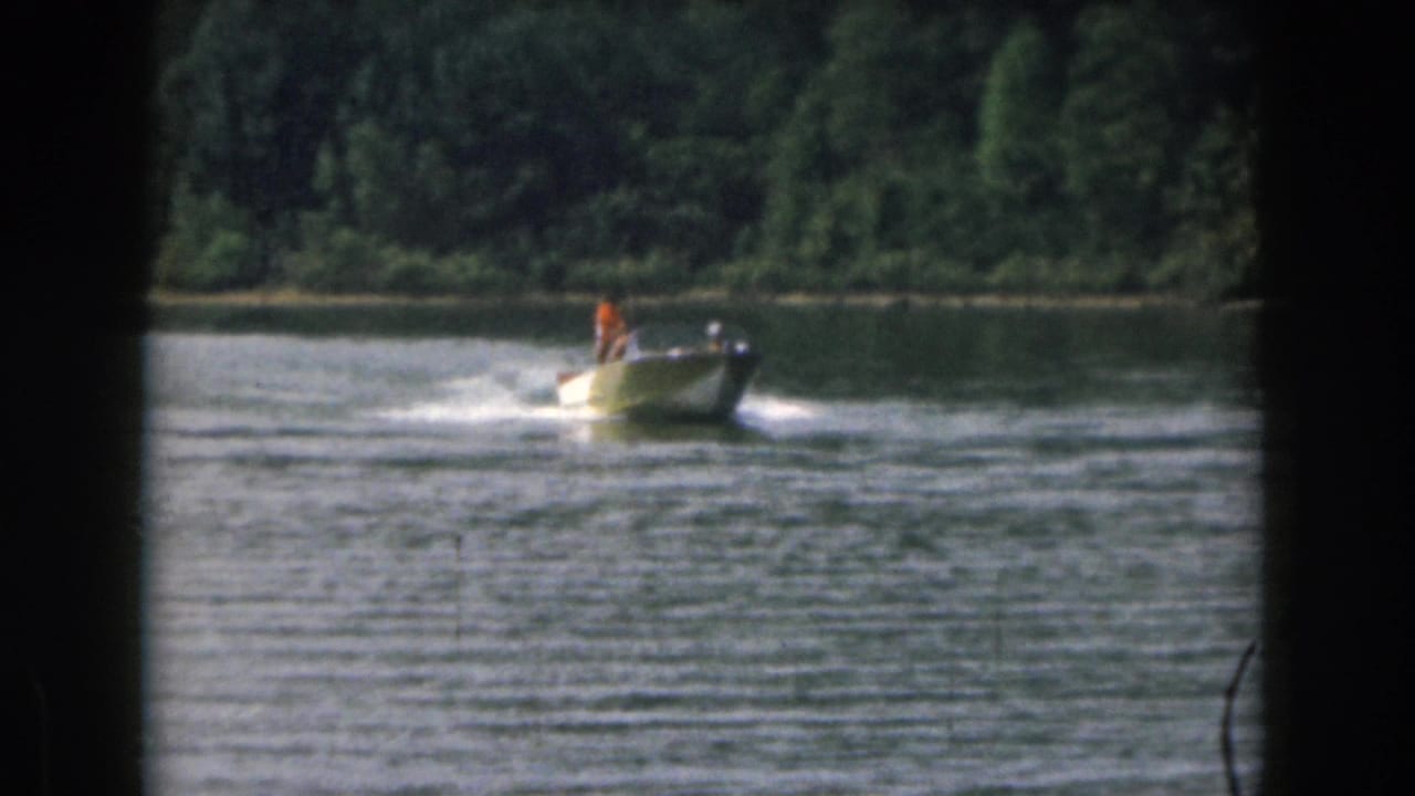 Small motorboat pulling a water skier across a lake with trees on the far shore.