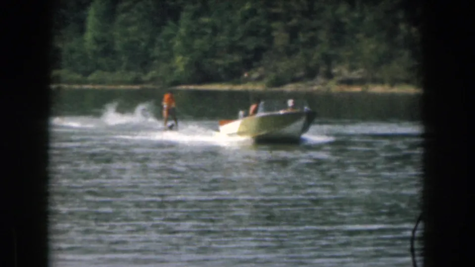 Grand Rapids area 1961 home-movie frame showing a water skier behind a small boat on a calm lake.