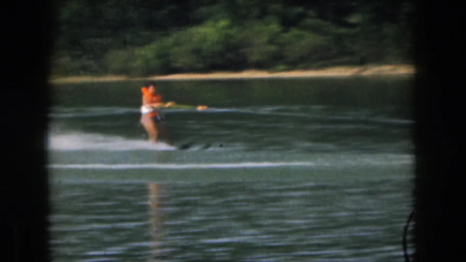 Final frame shows the woman water skier holding the tow handle on the lake, with wooded shoreline and 8mm frame shadows visible.