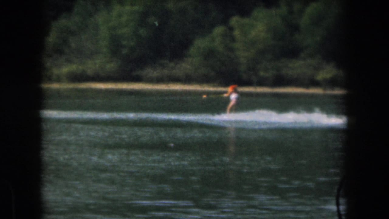 Water skier near the right side of the frame, skimming across lake water.