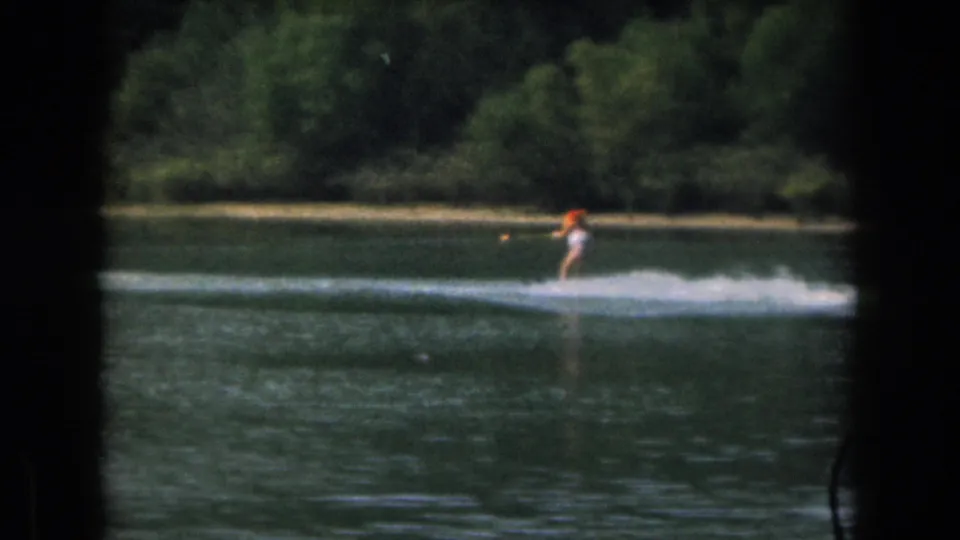 A distant skier in light clothing and an orange cap glides across the Grand Rapids lake scene, framed by dark 8mm borders.