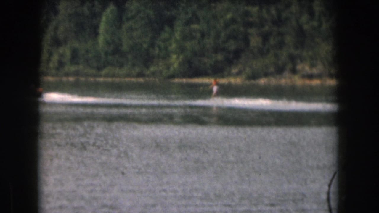Water skier gliding near the far shoreline with wake spread across the lake.
