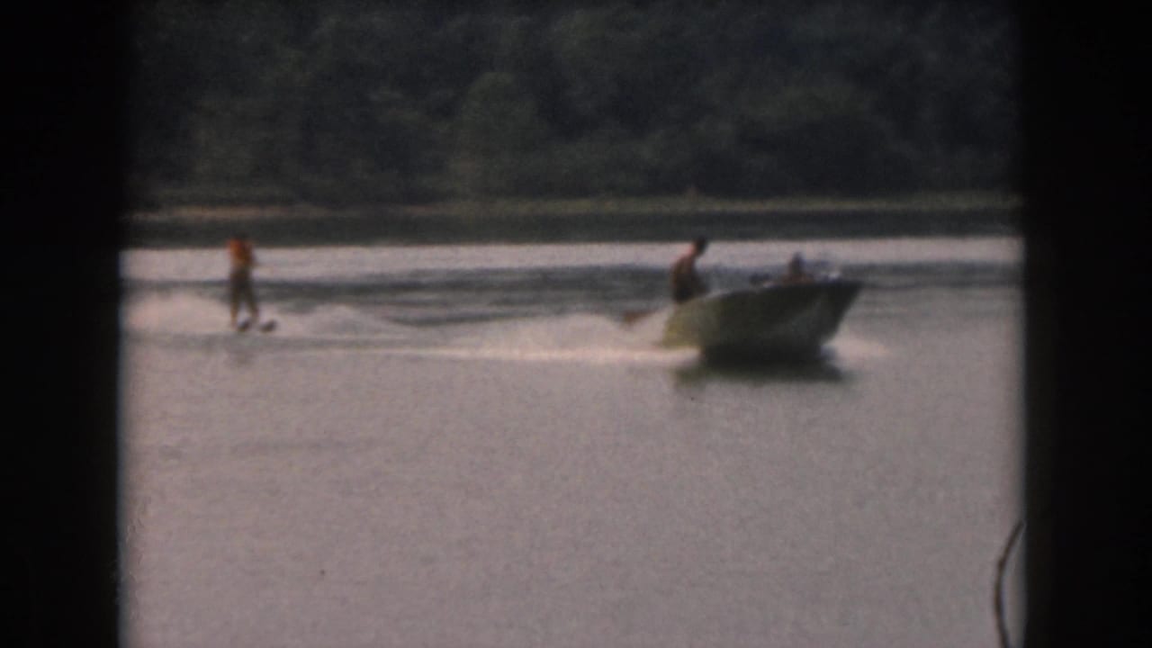 Water skier being pulled near a small motorboat on a calm lake.