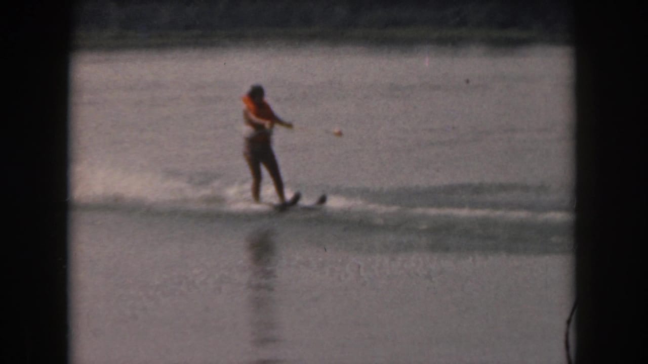 Woman on water skis holds a tow rope while moving across a lake.