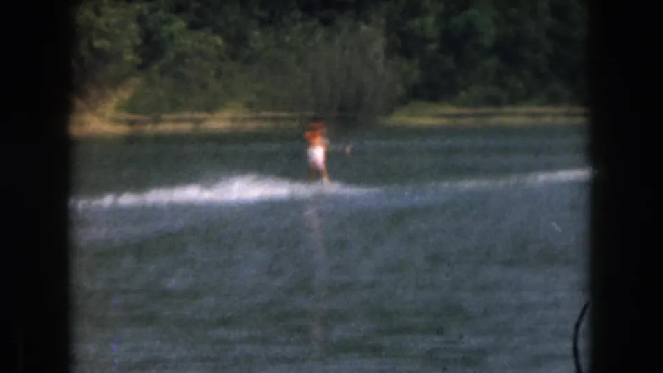 1961 Grand Rapids-area 8mm frame showing a distant water skier in a bright top moving across a tree-lined lake.