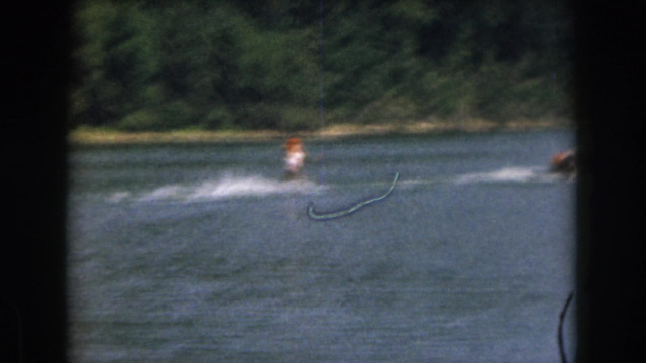 Water skier follows a speedboat across a lake, leaving a pale wake in the water.