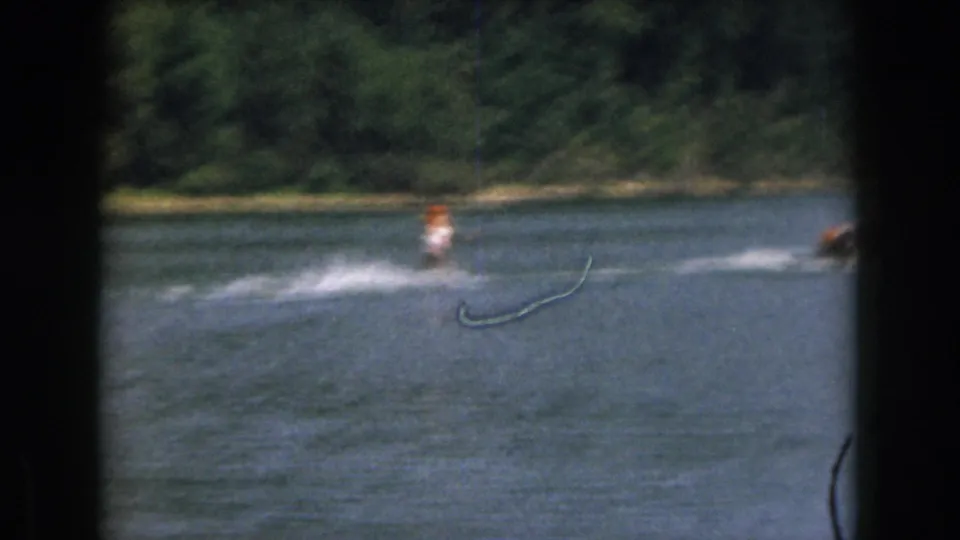 1961 Michigan home-movie frame with a distant skier being pulled across the lake behind a small speedboat.