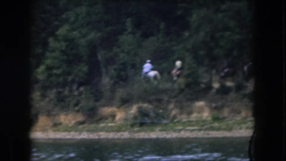 1961 Grand Rapids lakeside frame with riders partly obscured by trees along the far shore.