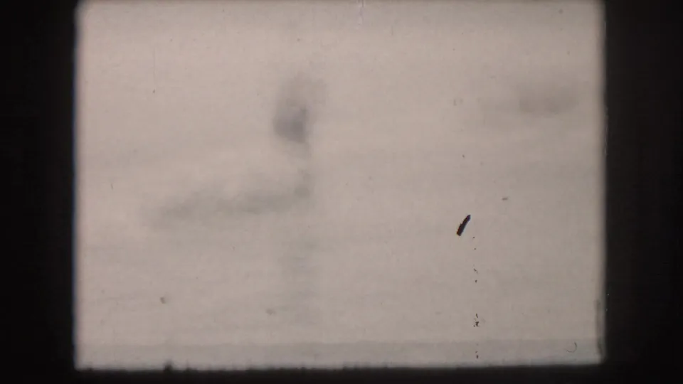 1961 home-movie frame from the Grand Rapids lake scene, showing washed lake water and soft shoreline detail between skiing moments.