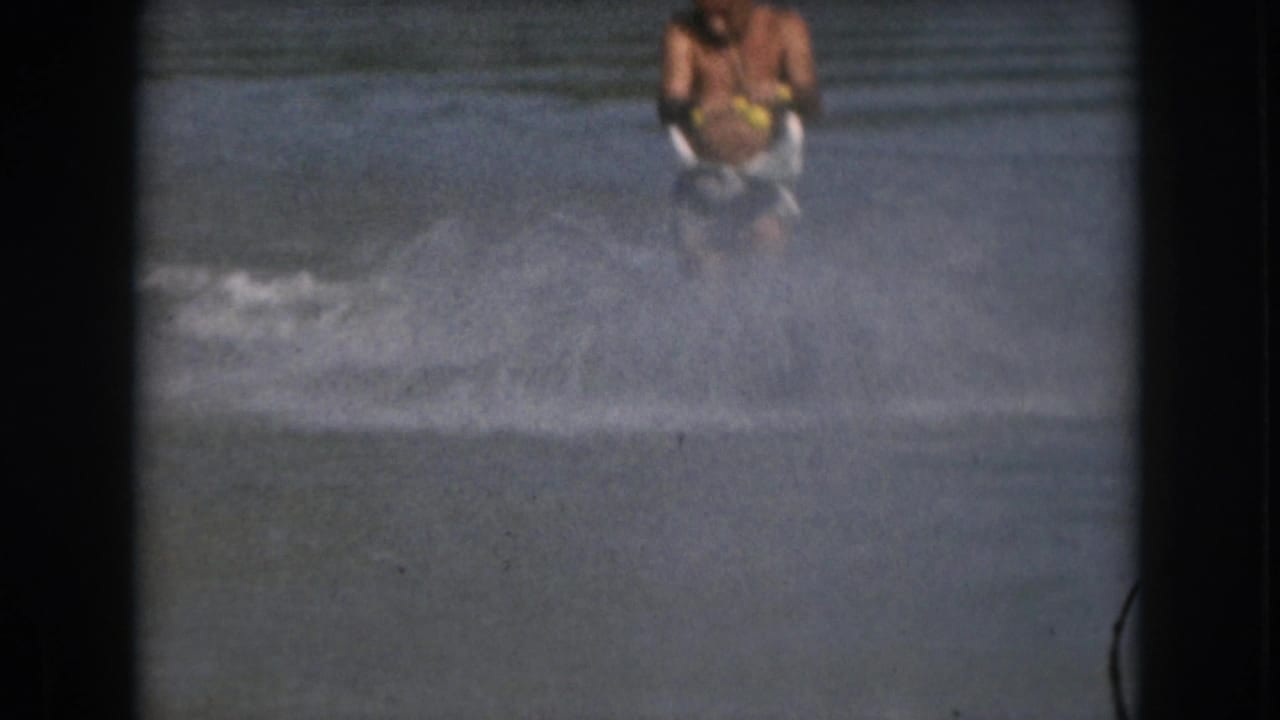 1961 Michigan frame with the skier partly hidden behind spray while holding the tow handle on open water.