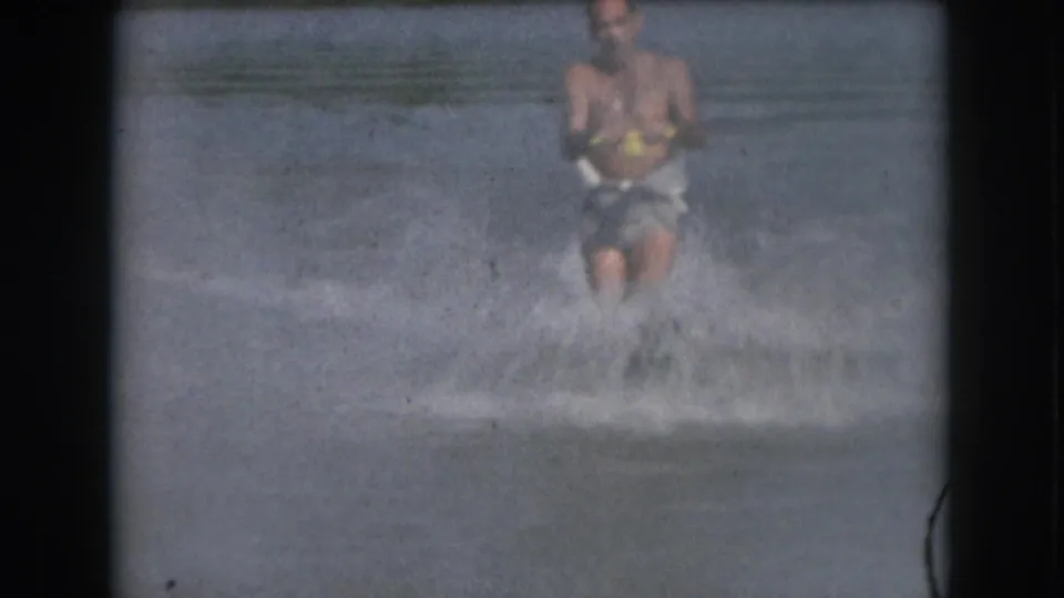 Soft 8mm frame from 1961 Michigan showing the skier centered behind spray with calm water visible beyond.