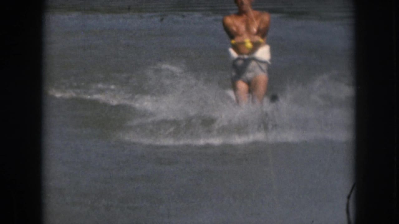 Adult man water skiing through open water with spray around his legs.