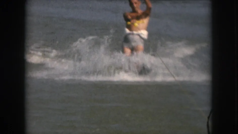 1961 Michigan 8mm frame showing an adult man water skiing through a burst of spray, with a tow rope cutting diagonally across the water.