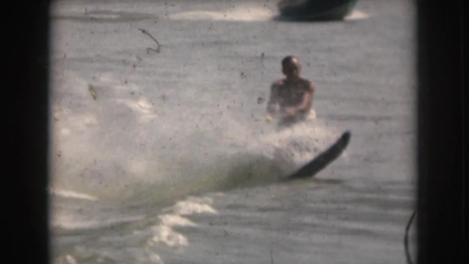 The skier is farther from camera as a boat appears in the background, suggesting the tow source on the lake.