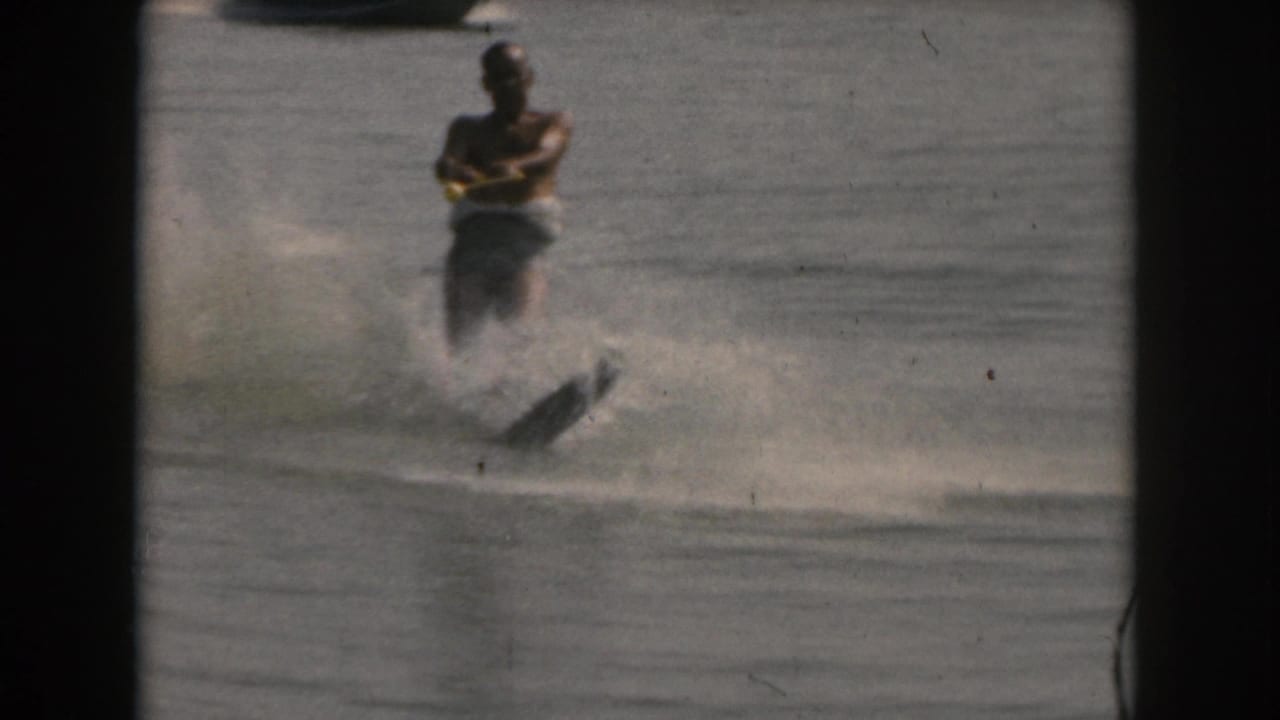 An adult man in a life vest continues a water-ski run on a lake in the Grand Rapids, Michigan area, with the single ski angled through spray in 8mm home-movie footage from 1961.