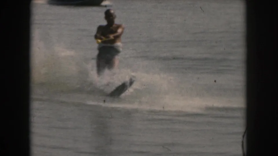 An adult man in a life vest continues a water-ski run on a lake in the Grand Rapids, Michigan area, with the single ski angled through spray in 8mm home-movie footage from 1961.
