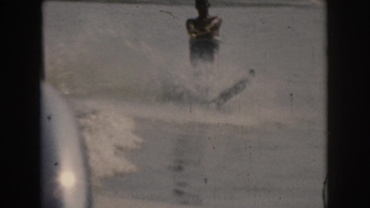 1961 Grand Rapids 8mm frame with a man on water skis moving through spray beside the boat wake on smooth water.